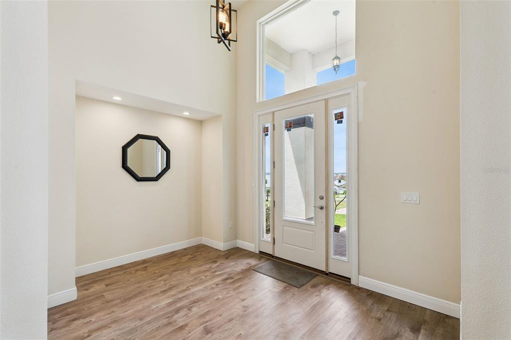 A bright entryway features wood-look flooring, a high ceiling, a front door, and a mirror — 1837 MOORINGS COURT, CLERMONT, FL