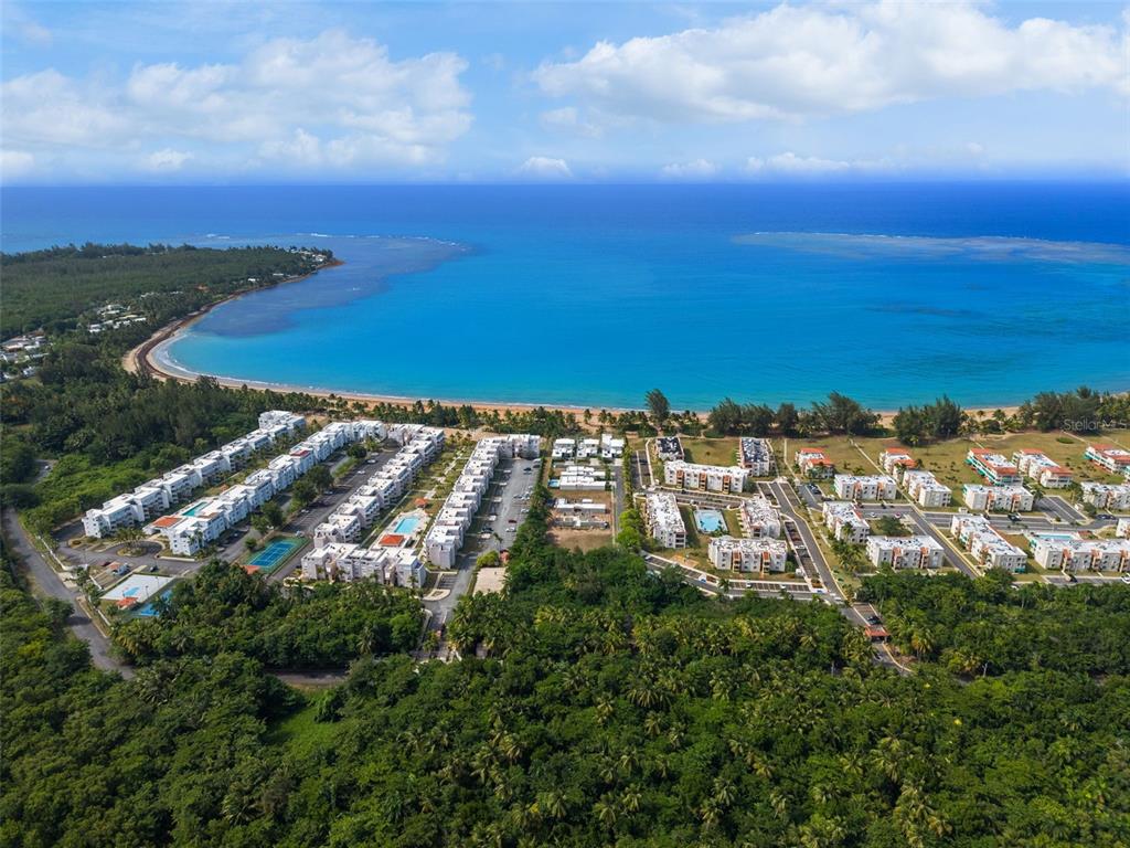 An aerial view shows a coastal residential complex with white buildings near a sandy beach — OCEAN FOREST Lot 2, RIO GRANDE, PR