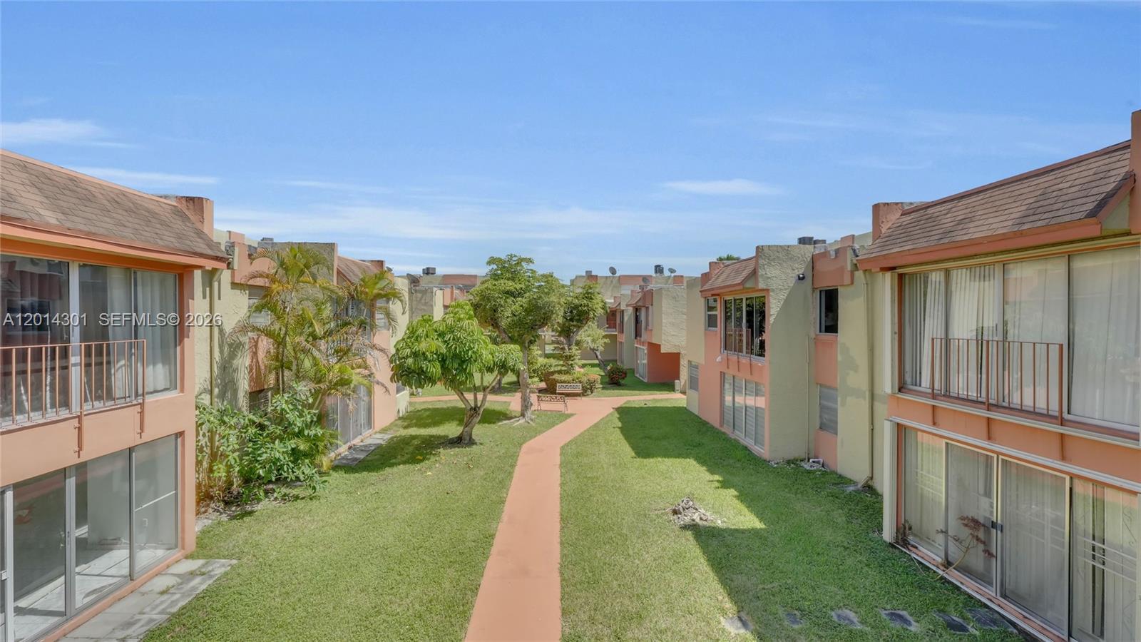 An exterior view of a courtyard between two-story residential buildings with balconies and green lawns — 9390 W Flagler St # 210A, Miami FL 33174, MIAMI, FL