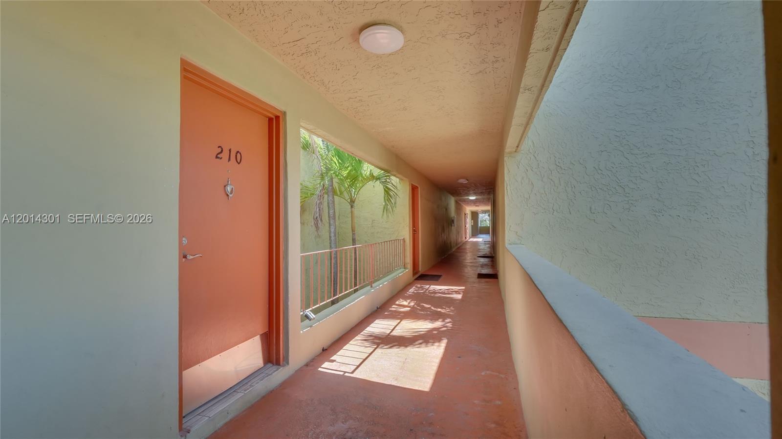 An outdoor apartment building hallway features orange doors, a concrete floor, and a metal railing — 9390 W Flagler St # 210A, Miami FL 33174, MIAMI, FL