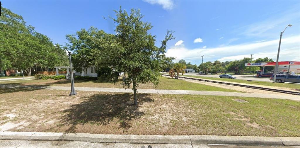 A grassy lot with a tree and sidewalk sits next to railroad tracks and a gas station — N/A, LAKE WALES, FL
