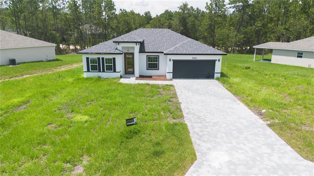 A single-story house with a white exterior, dark roof, and paved driveway sits on grass — 13265 SW 85TH CIRCLE, OCALA, FL