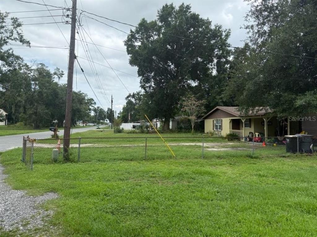 A fenced, grassy lot sits next to a small, single-story house under a cloudy sky — 5634 LORRAINE STREET, LAKELAND, FL