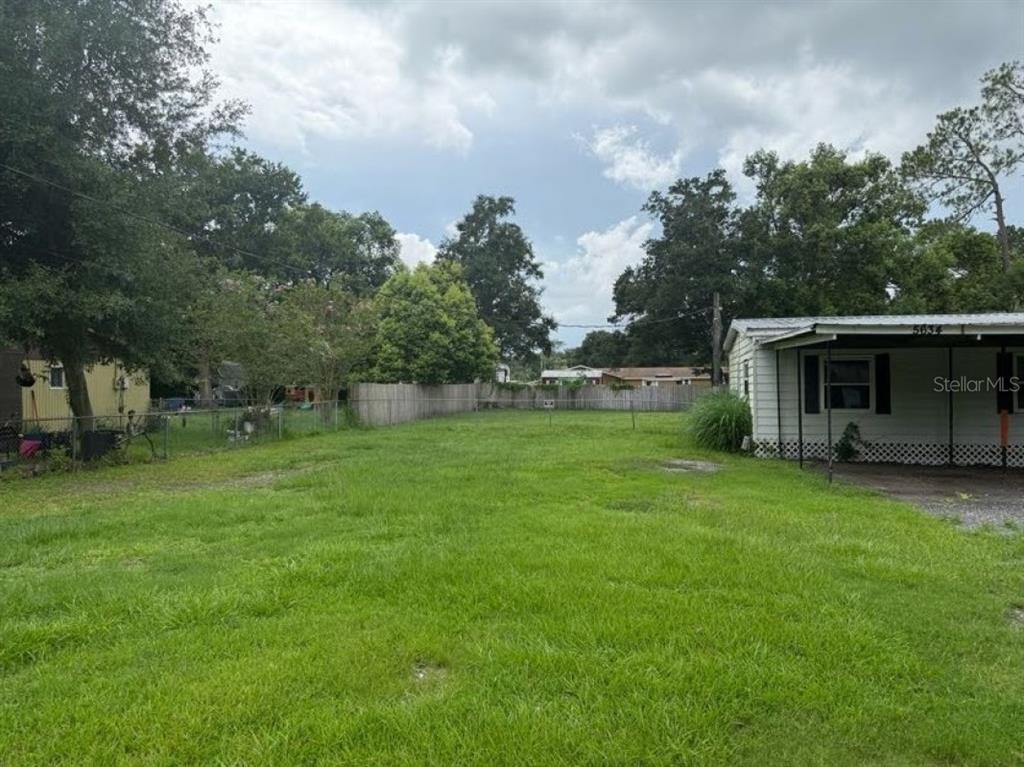 A grassy backyard sits between a mobile home and a wooden fence under a cloudy sky — 5634 LORRAINE STREET, LAKELAND, FL