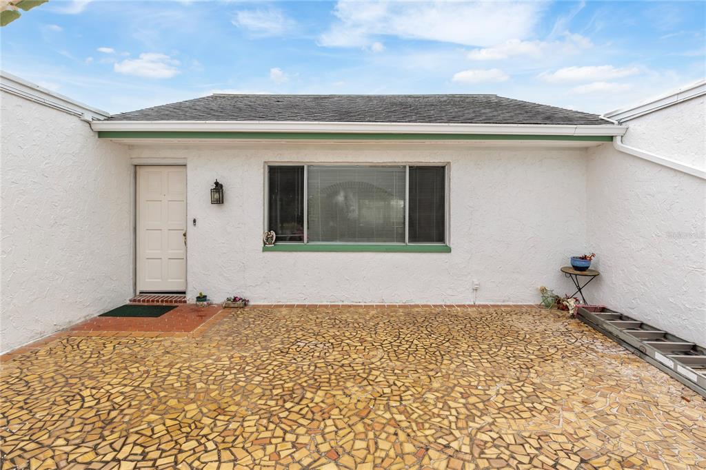 A white stucco house exterior features a mosaic-tiled patio, a front door, and a window — 3228 ROCK VALLEY DRIVE, HOLIDAY, FL