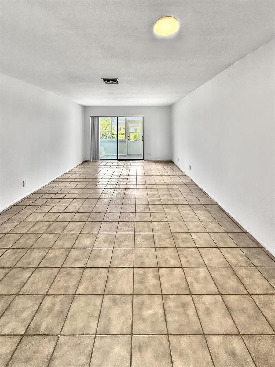 An empty room with beige tile flooring, white walls, and a sliding glass door — 5263 Cresthaven Boulevard # A, West Palm Beach FL 33415, WEST PALM BEACH, FL
