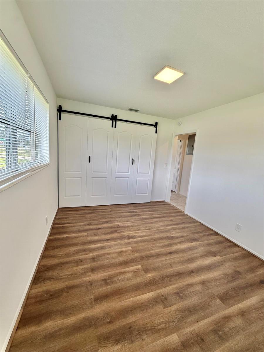 An empty room features wood-look flooring, white walls, a window with blinds, and sliding barn doors — 5263 Cresthaven Boulevard # A, West Palm Beach FL 33415, WEST PALM BEACH, FL