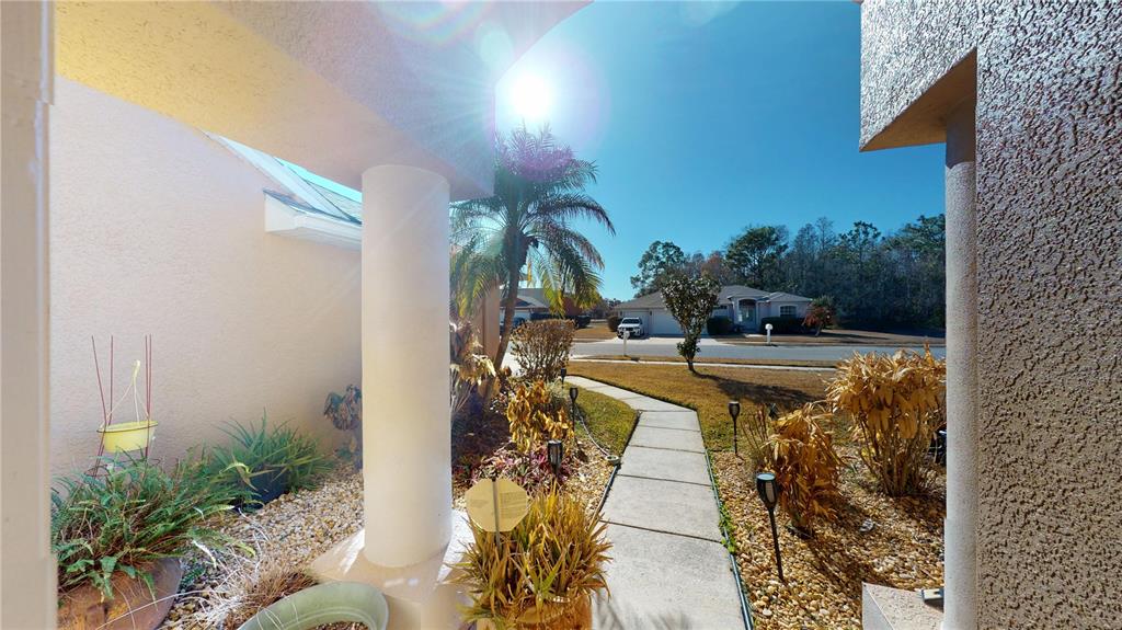 A concrete walkway leads from a covered porch toward a suburban street and house — 6942 ORVICTI COURT, WESLEY CHAPEL, FL