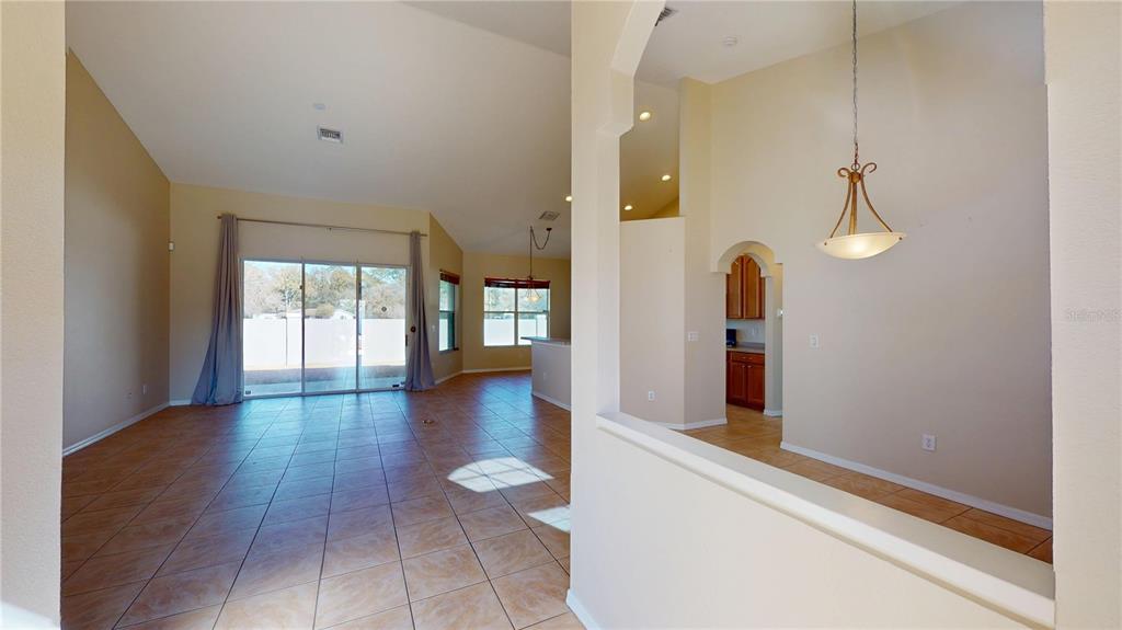 An open-concept living area features tile flooring, vaulted ceilings, and a view into the kitchen — 6942 ORVICTI COURT, WESLEY CHAPEL, FL