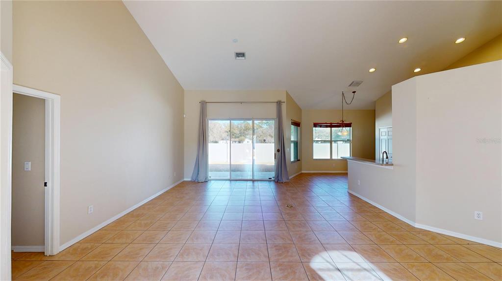 An open-concept living area features vaulted ceilings, tile flooring, and sliding glass doors to outside — 6942 ORVICTI COURT, WESLEY CHAPEL, FL