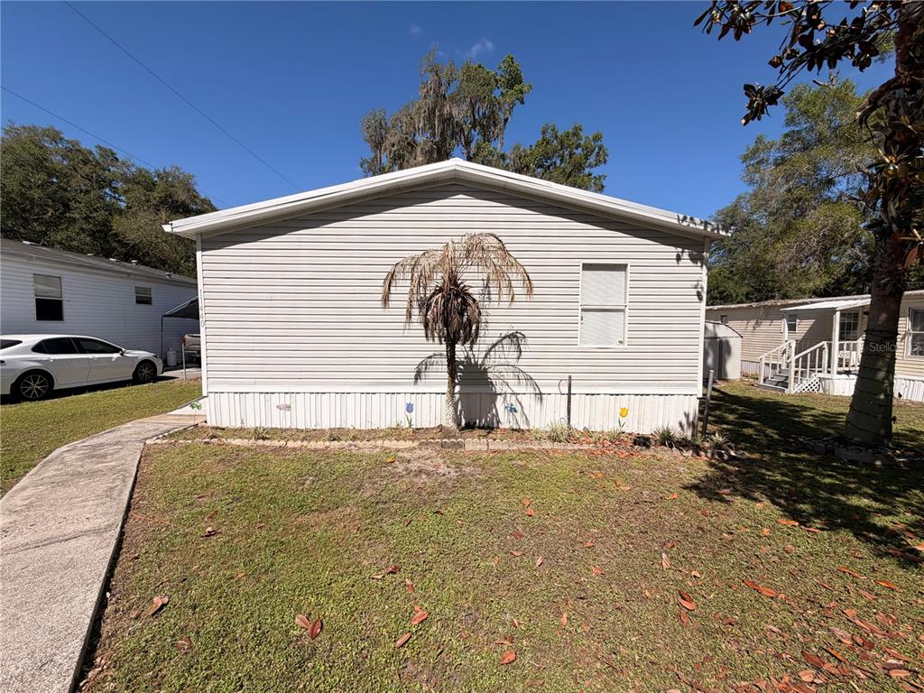 The exterior side view of a light-colored manufactured home features a small palm tree — 11440 CR 675W, WEBSTER, FL