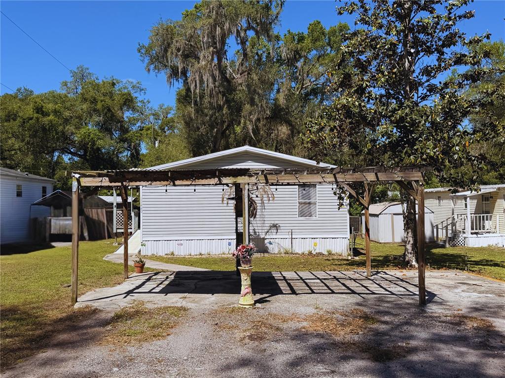 A light-colored mobile home features a wooden pergola covering a concrete driveway area — 11440 CR 675W, WEBSTER, FL