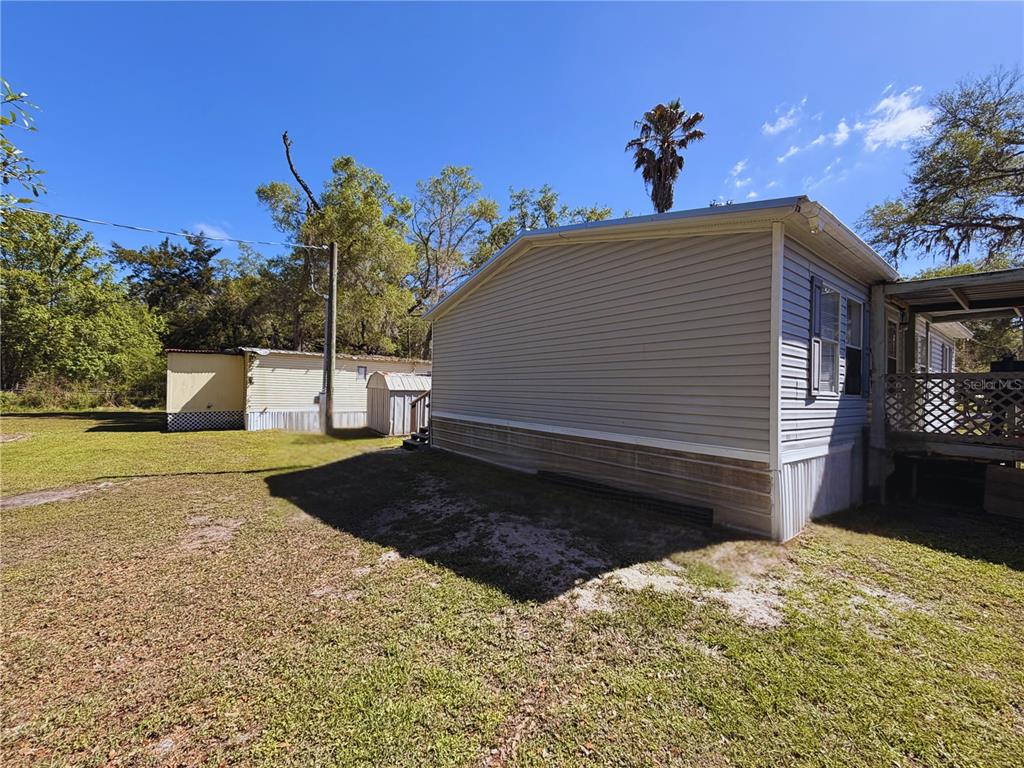 A side view of a light-colored mobile home with a wooden deck and adjacent shed — 11440 CR 675W, WEBSTER, FL