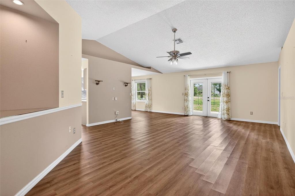 A spacious living room features wood-look flooring, vaulted ceilings, and glass doors leading outside — 2127 KING RICHARDS COURT, ORANGE CITY, FL