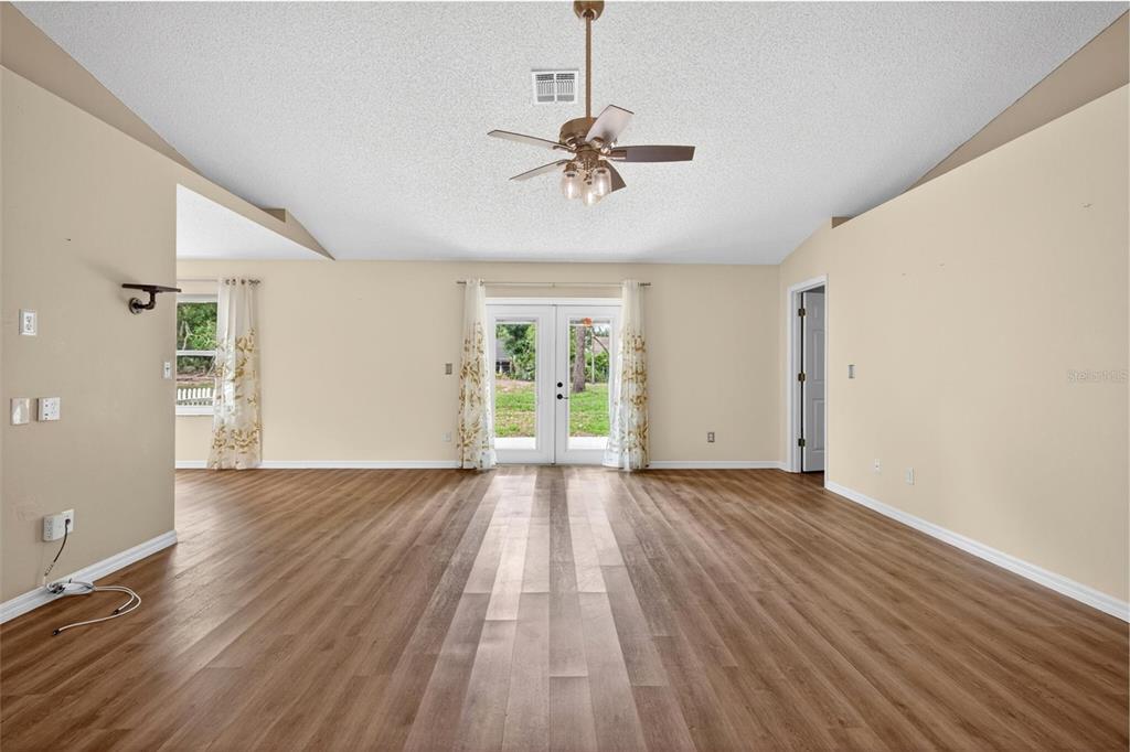 A spacious living room features light-colored walls, wood-look flooring, a ceiling fan, and glass doors — 2127 KING RICHARDS COURT, ORANGE CITY, FL