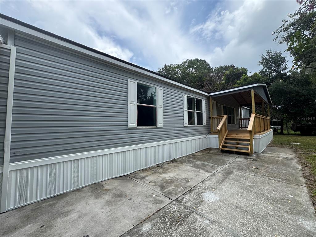 The exterior of a gray manufactured home features a concrete patio and a wooden porch — 4804 KIPP CIRCLE, PLANT CITY, FL