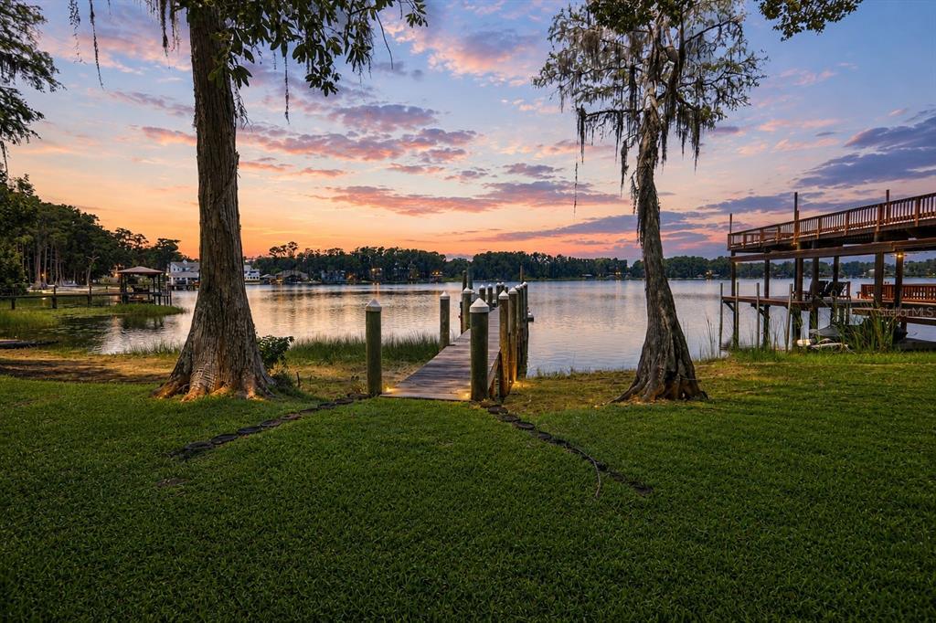A wooden dock extends into a lake at sunset, framed by two large trees — 17810 CRAWLEY ROAD, ODESSA, FL