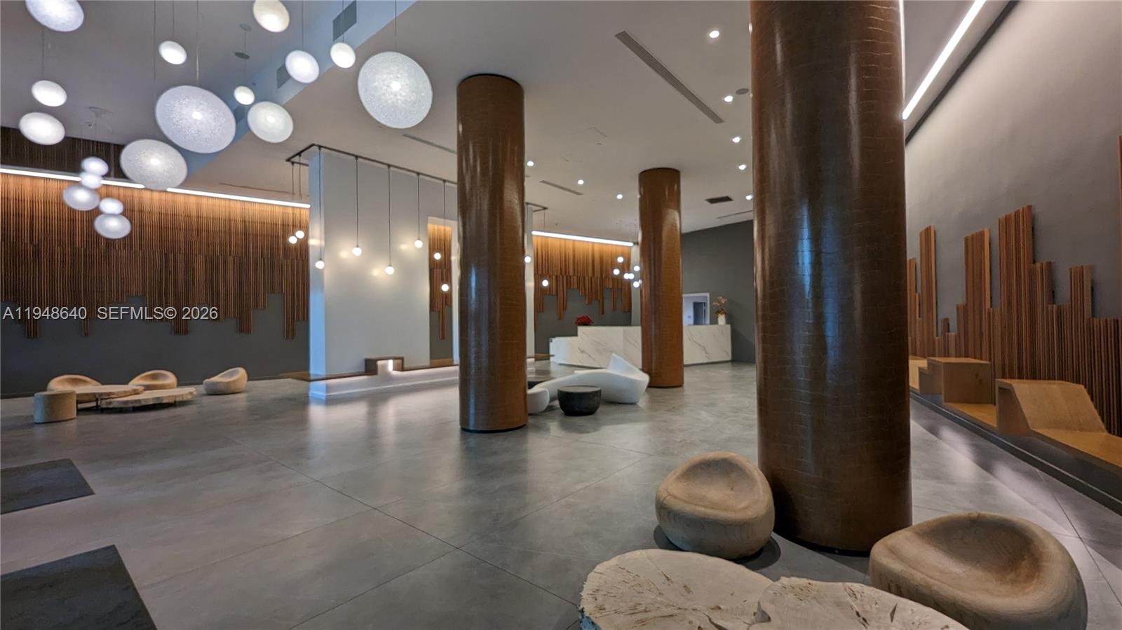 A modern lobby features large cylindrical columns, wood slat wall accents, and spherical pendant lights — 350 S Miami Ave # 702, Miami FL 33130, MIAMI, FL
