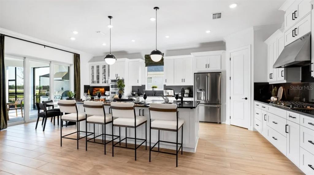A modern kitchen features white cabinetry, a large island with four stools, and wood-look flooring — 26789 VICTORIA PLACE, PUNTA GORDA, FL