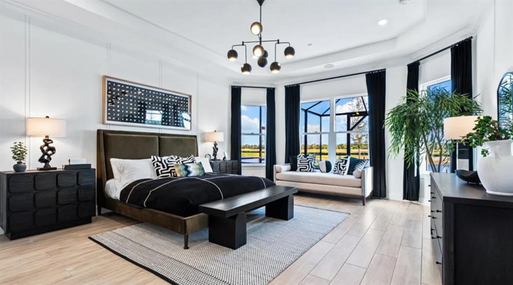 A modern bedroom features a dark upholstered bed, a bench, and large windows overlooking outdoors — 26789 VICTORIA PLACE, PUNTA GORDA, FL