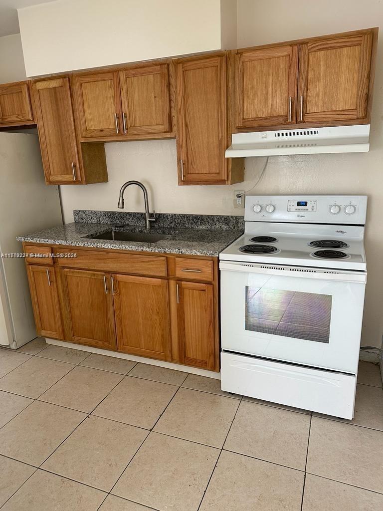 A kitchen features light wood cabinets, granite countertops, and a white electric range — 756 NW 5th St, Hallandale Beach FL 33009, HALLANDALE BEACH, FL