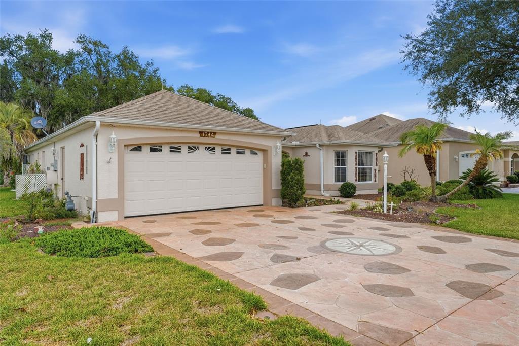 A single-story house with a white garage door and a decorative stone-patterned concrete driveway — 1344 AUGUSTINE DRIVE, THE VILLAGES, FL