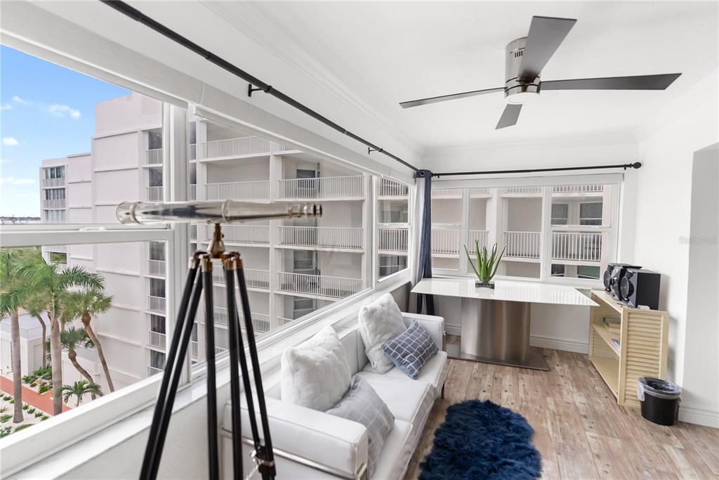 A sunroom features a white sofa, a modern desk, a telescope, and views of buildings — 1750 BENJAMIN FRANKLIN DRIVE UNIT 6G, SARASOTA, FL