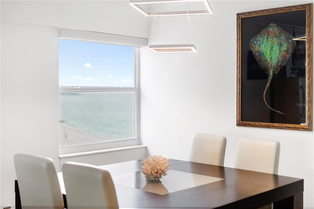 A dining room features a dark wood table, white chairs, and a view of the ocean — 1750 BENJAMIN FRANKLIN DRIVE UNIT 6G, SARASOTA, FL