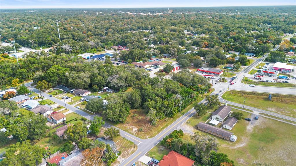 An aerial view shows a wooded lot situated between residential streets and commercial properties — 905 W BERESFORD AVENUE, DELAND, FL