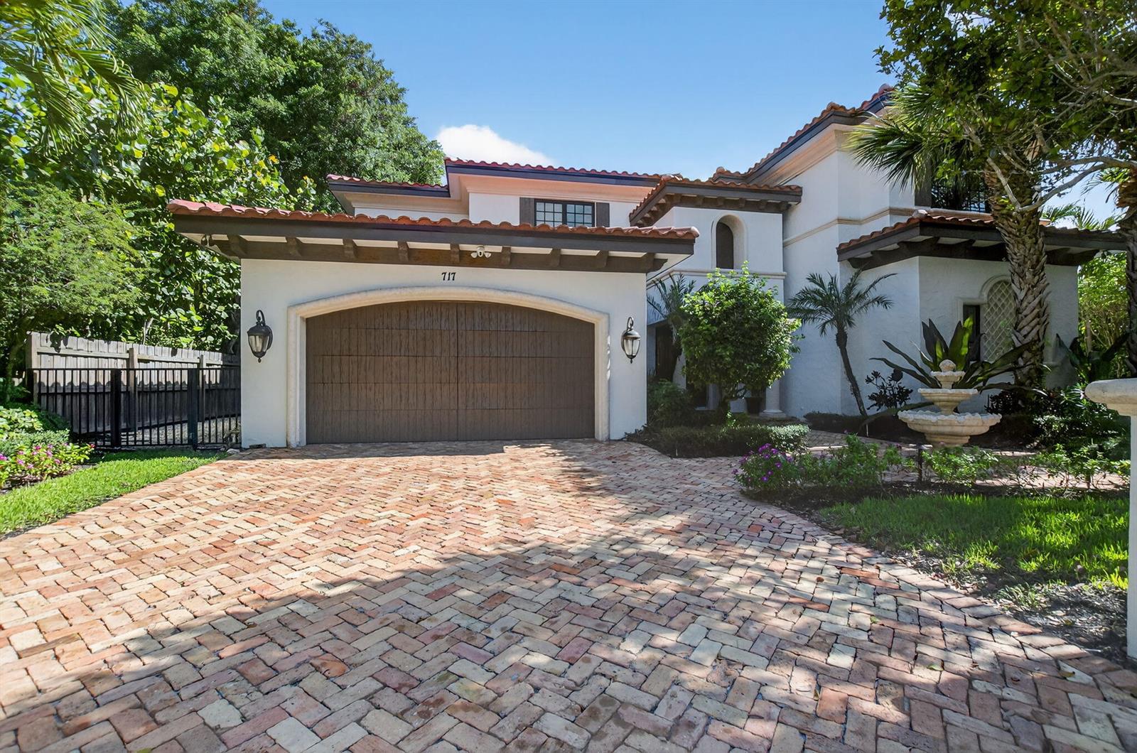 A three-tiered stone fountain sits on a brick walkway in front of a Mediterranean-style home — 717 NW 4th Street, Boca Raton FL 33486, BOCA RATON, FL