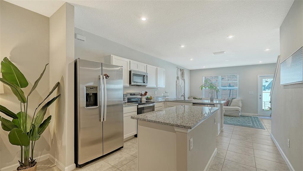 A modern kitchen features white cabinetry, granite countertops, stainless steel appliances, and an island — 14147 CRIMSON AVENUE, BRADENTON, FL