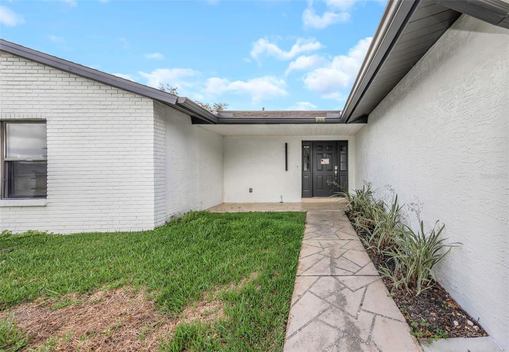 A white brick house exterior features a stone walkway leading to a dark front door — 4030 FIELDGREEN PLACE, LAND O LAKES, FL