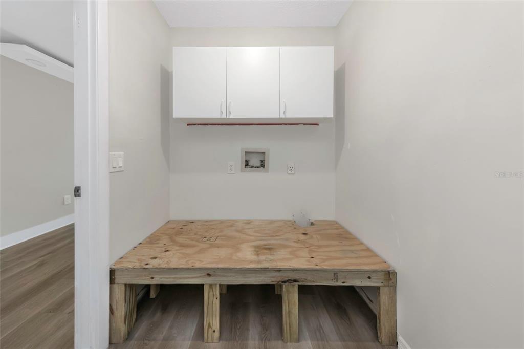 A laundry room features a raised wooden platform, white wall cabinets, and utility connections — 4030 FIELDGREEN PLACE, LAND O LAKES, FL