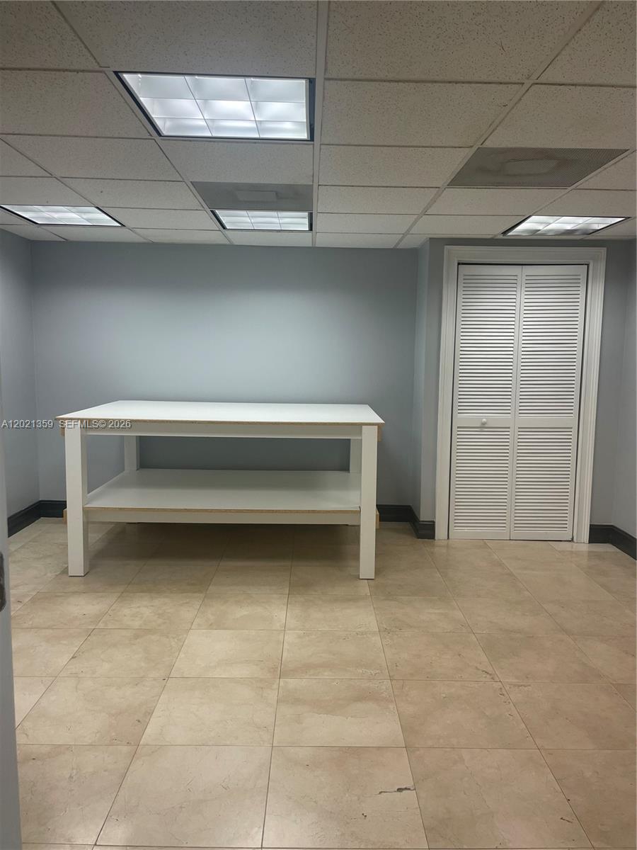 A room with light-colored tile flooring, a white work table, and a louvered closet door — MIAMI, FL