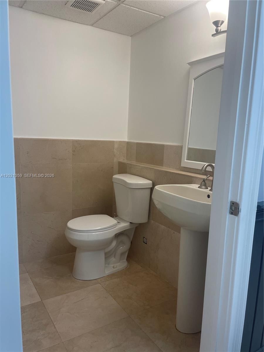 A small bathroom features a pedestal sink, a toilet, and beige tiled walls and floors — MIAMI, FL