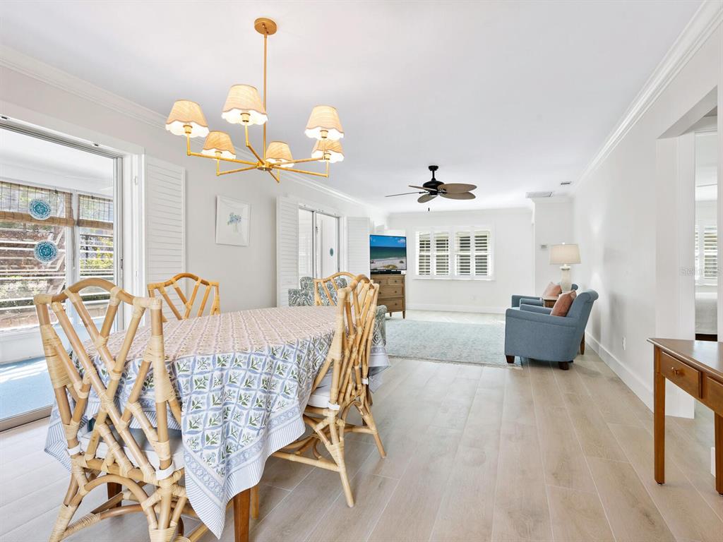 A dining area with bamboo chairs and a chandelier opens into a living room space — 1214 MOONMIST CIRCLE UNIT S-01S, SARASOTA, FL