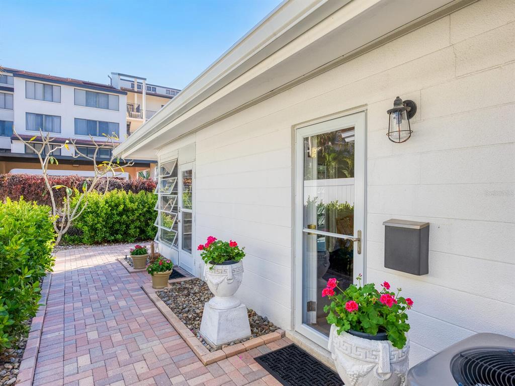 A paved walkway leads past two glass doors and potted flowers along a white wall — 1214 MOONMIST CIRCLE UNIT S-01S, SARASOTA, FL