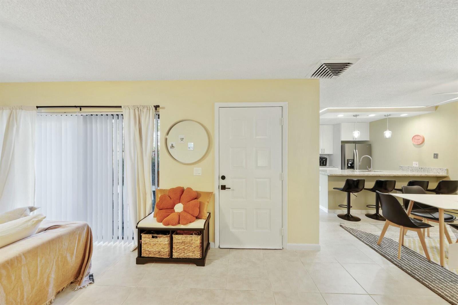 A living room with a white door, a storage bench, and an adjacent open kitchen — 5110 51st Way, West Palm Beach FL 33409, WEST PALM BEACH, FL