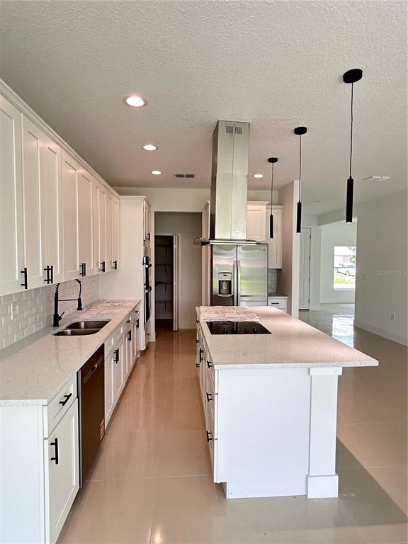 A modern kitchen features white cabinets, a central island with a cooktop, and stainless appliances — 286 CATALONIA AVENUE NW, PALM BAY, FL
