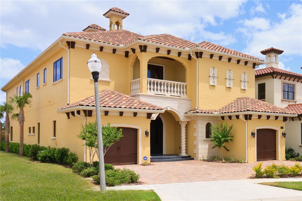 A two-story yellow stucco house features a tile roof, arched entryway, and two garage doors — 7825 PALMILLA COURT, REUNION, FL