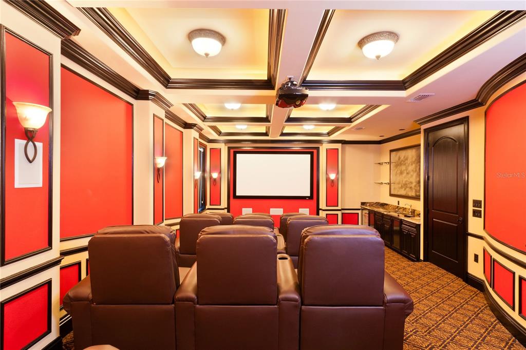 A home theater room features tiered brown leather seating, a projector screen, and red walls — 7825 PALMILLA COURT, REUNION, FL