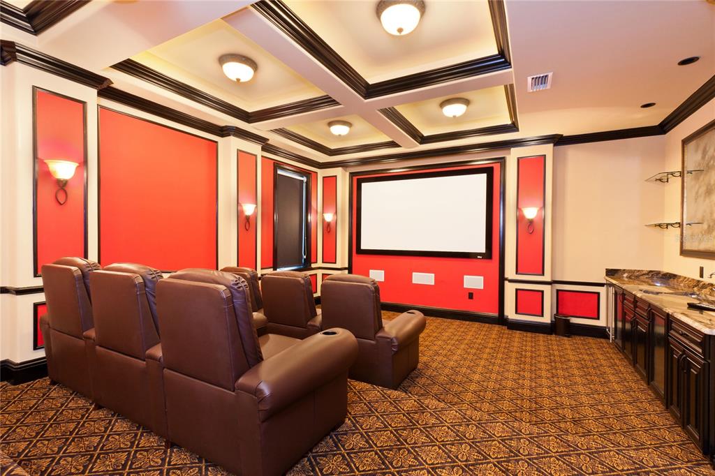 A home theater features brown leather recliners, a projector screen, red walls, and coffered ceilings — 7825 PALMILLA COURT, REUNION, FL