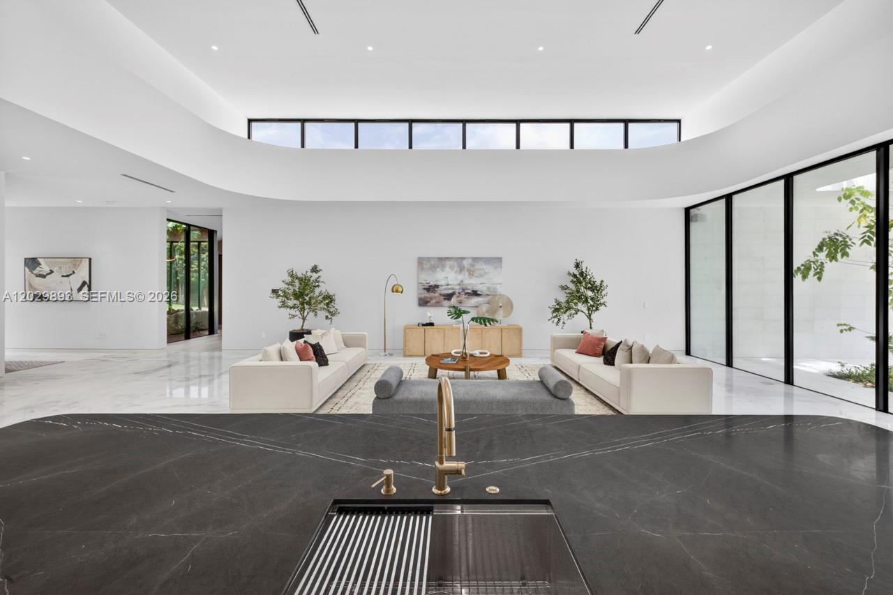 A modern kitchen island with a dark stone countertop overlooks a spacious, minimalist living area — 5671 SW 130th Ave, Southwest Ranches FL 33330, SOUTHWEST RANCHES, FL