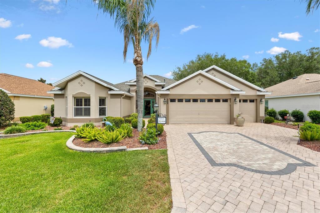 A single-story house with a beige stucco exterior, a paver driveway, and a palm tree — 1816 BLYTHEWOOD LOOP, THE VILLAGES, FL