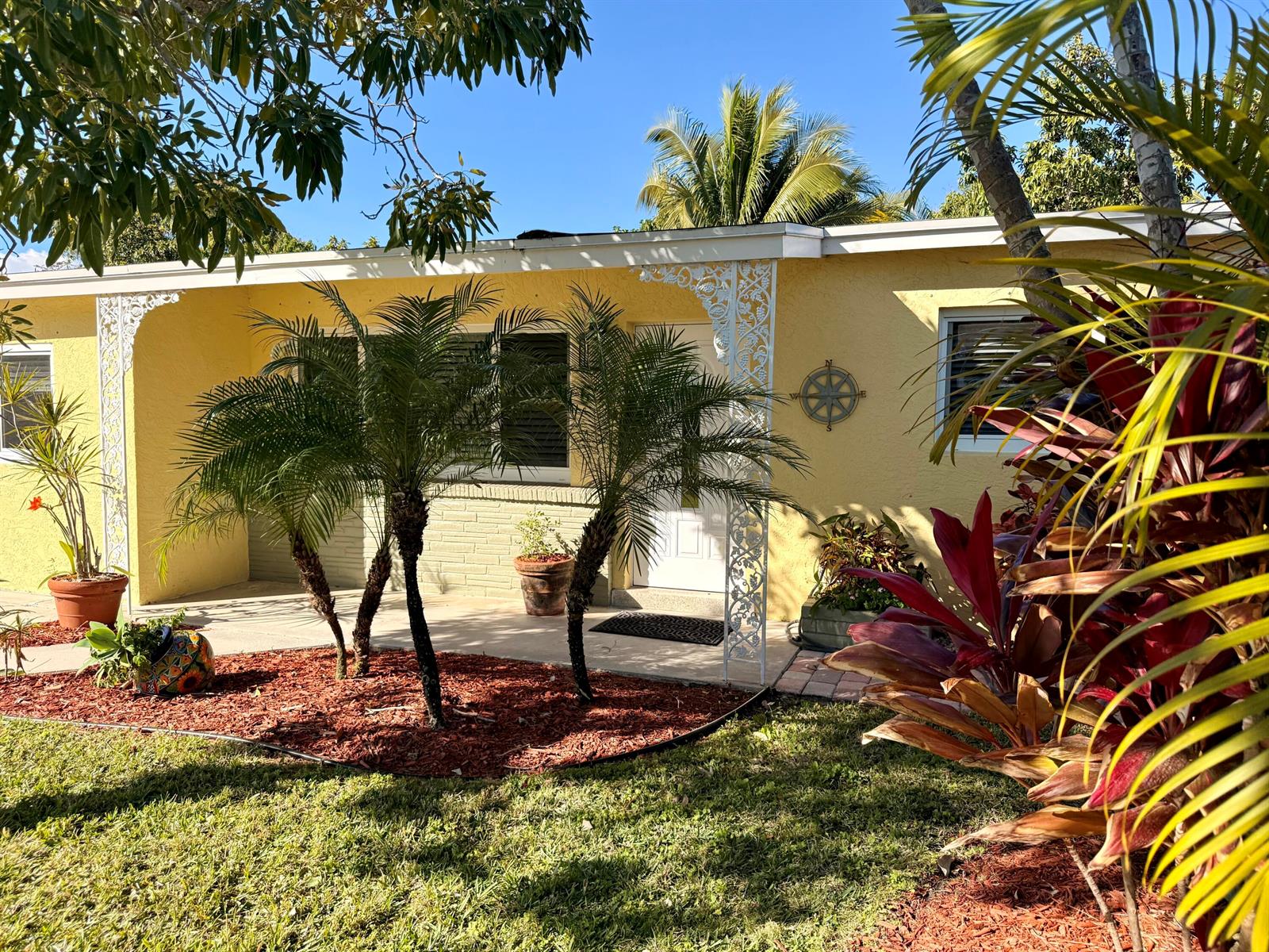A yellow single-story house features white decorative porch brackets, palm trees, and a front garden — 607 W Perry Street, Lantana FL 33462, LANTANA, FL