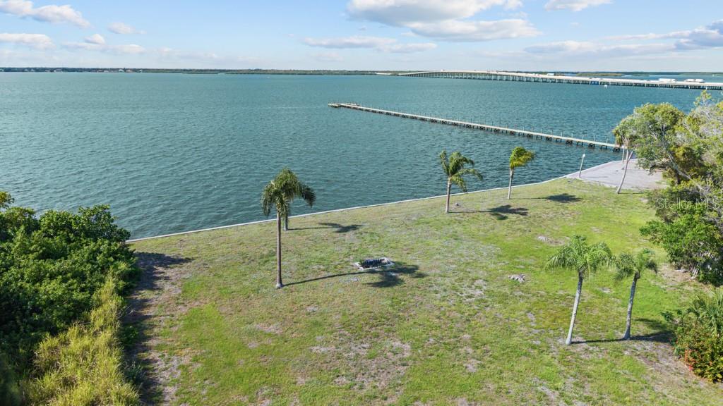 An aerial view shows a grassy waterfront lot with palm trees and a long wooden pier — 26014 SHORE DRIVE, PUNTA GORDA, FL