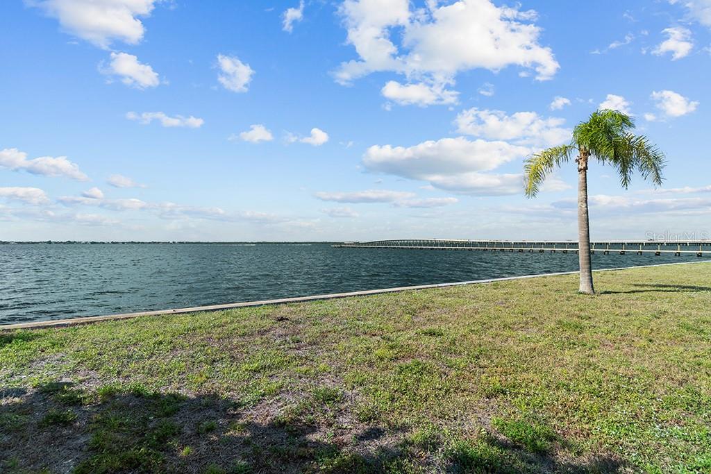 A palm tree stands on a grassy lawn overlooking a lake with a long pier — 26014 SHORE DRIVE, PUNTA GORDA, FL