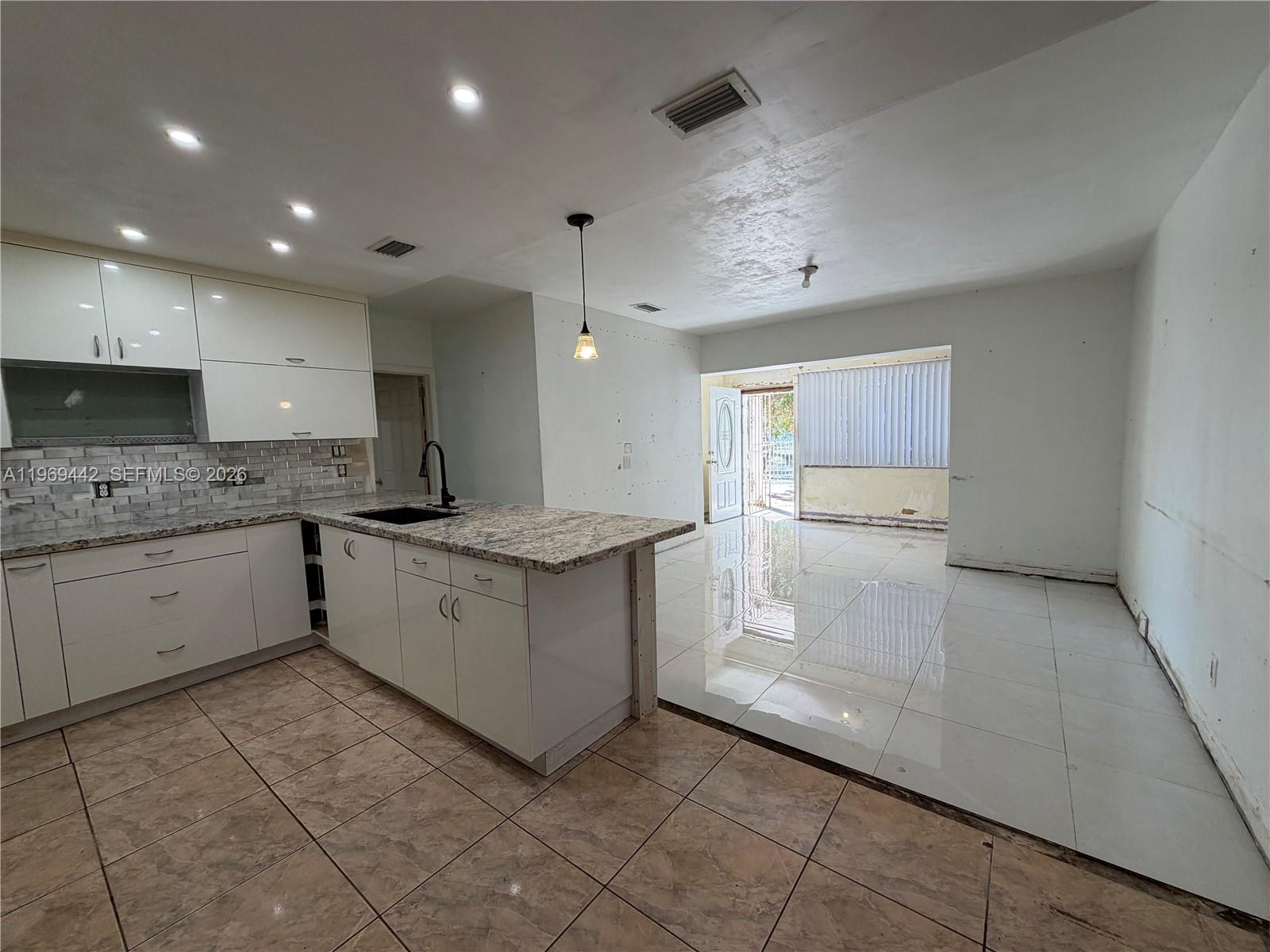 A kitchen with white cabinets and granite countertops transitions to a tiled living area — 14015 NE 11th Ave, North Miami FL 33161, NORTH MIAMI, FL
