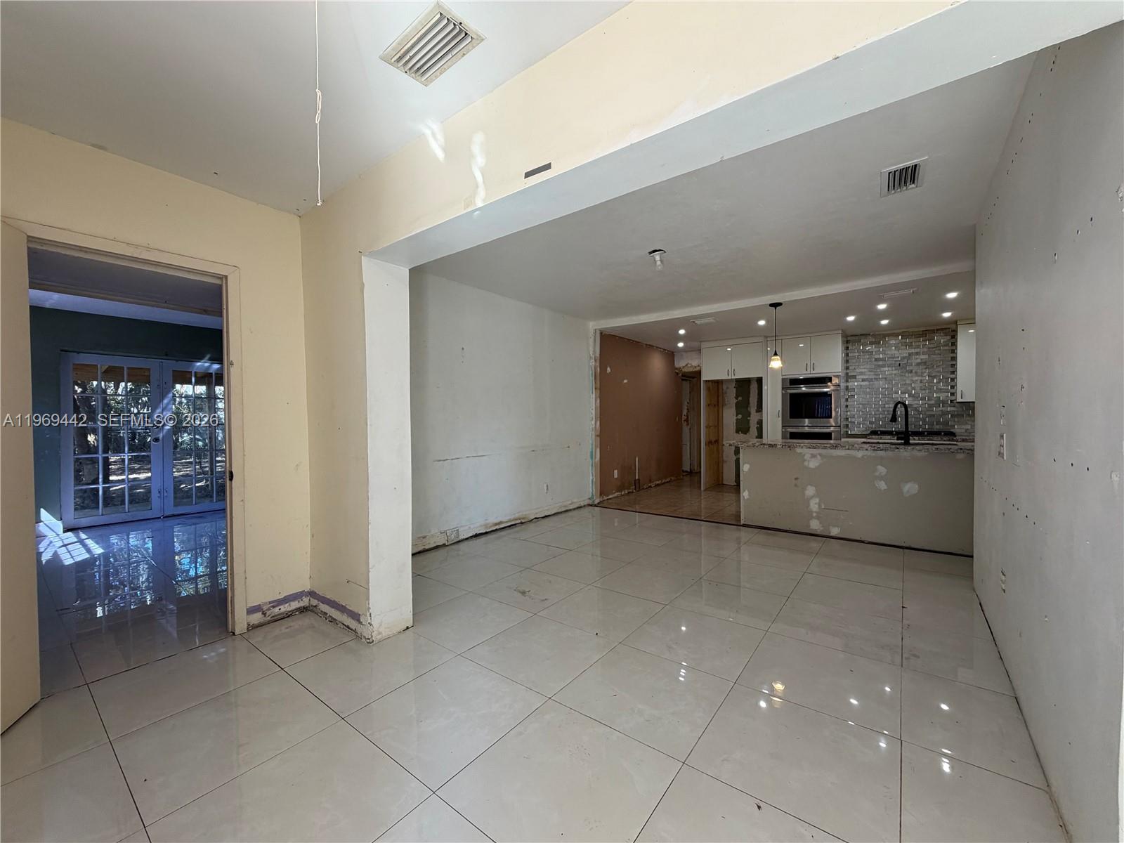 An open-concept living area features large light-colored floor tiles and an unfinished kitchen space — 14015 NE 11th Ave, North Miami FL 33161, NORTH MIAMI, FL