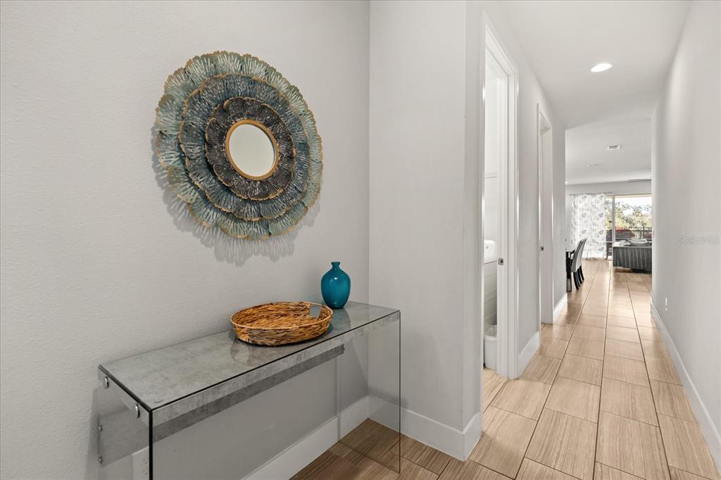 A hallway features a glass console table, a decorative wall mirror, and light tile flooring — 1113 CASTLE PINES COURT, REUNION, FL